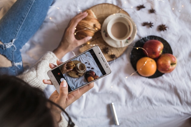 Foto de mujer tomando café y frutas con smartphone