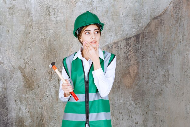 Foto de mujer trabajadora de la construcción en casco verde sosteniendo un martillo