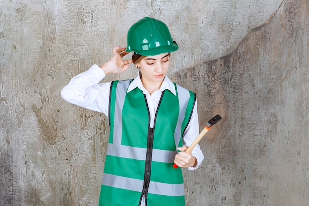 Foto de mujer trabajadora de la construcción en casco verde sosteniendo un martillo