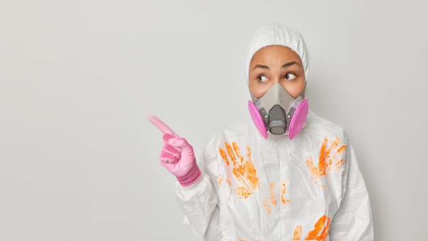 La foto de una mujer vestida con un traje protector de materiales peligrosos apunta hacia un espacio en blanco y anuncia que algo muestra la dirección que queda aislada sobre un fondo gris Modelo femenino con traje de radiación se encuentra en el interior