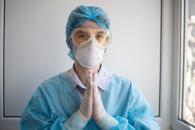 Foto de una mujer vistiendo un equipo de protección de personal médico y rezando