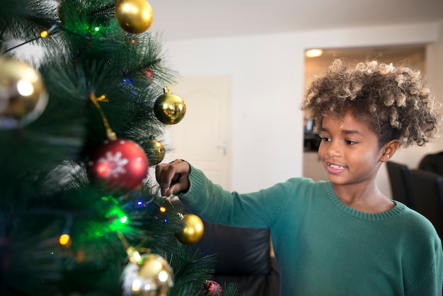 Foto de una niña afroamericana con pelo rizado decorando el árbol de Navidad en el salón