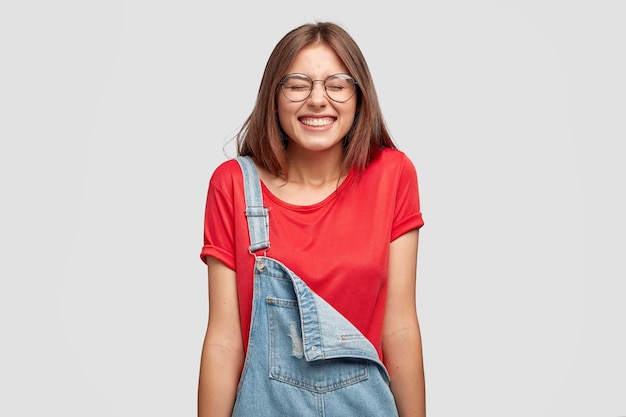 Foto gratuita foto de una niña feliz de aspecto agradable que se ríe positivamente, entrecierra los ojos, se ríe de una broma divertida