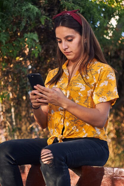 Foto de una niña mirando su teléfono mientras está sentada en el banco