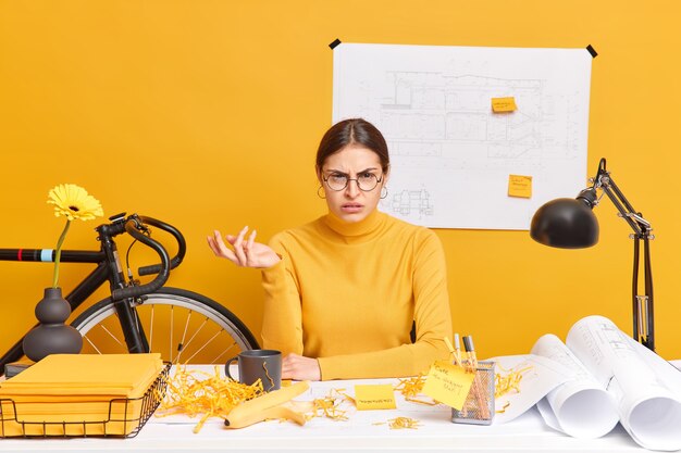 Foto de oficinista mujer indignada insatisfecha encoge de hombros no sabe cómo terminar el trabajo del proyecto. La diseñadora estudiante trabaja en poses de dibujos en el espacio de coworking. Concepto de educación