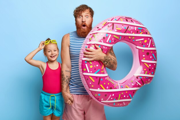 Foto de padre e hija de jengibre estupefactos posando en trajes de piscina