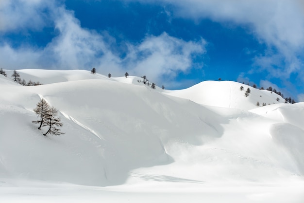 Foto de paisaje de colinas cubiertas de nieve en un nublado cielo azul