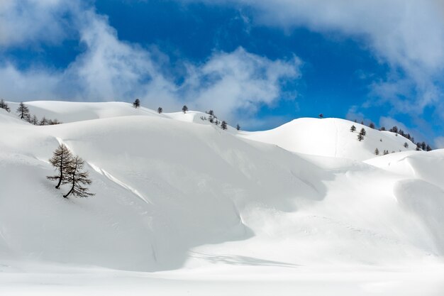 Foto de paisaje de colinas cubiertas de nieve en un nublado cielo azul