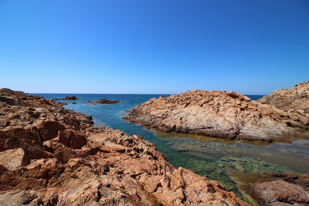 Foto de paisaje de una orilla del mar con grandes rocas en un cielo azul claro