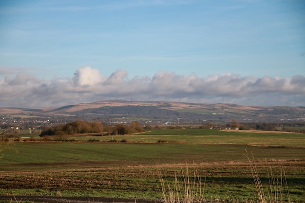 Foto panorámica de campos verdes y colinas bajo un cielo azul nublado