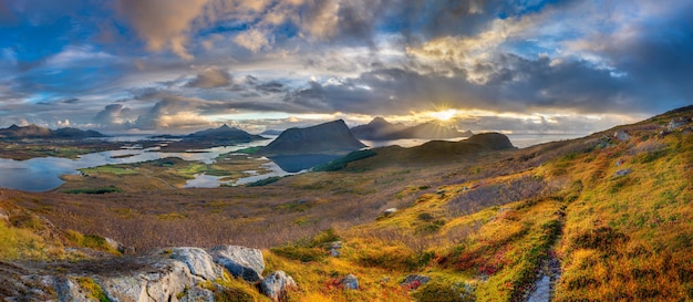 Foto panorámica de colinas cubiertas de hierba y montañas cerca del agua bajo un cielo nublado azul en Noruega