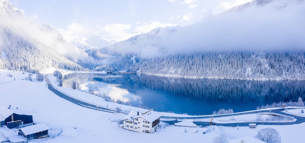 Foto panorámica de hermosos árboles cubiertos de nieve con un lago tranquilo bajo un cielo brumoso