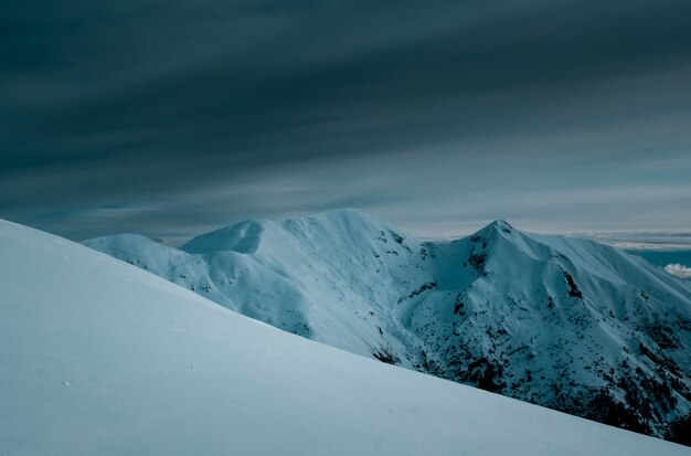 Foto panorámica de los picos de las montañas cubiertas de nieve bajo un cielo nublado