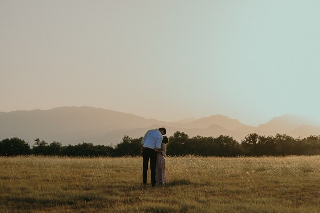Una foto de una pareja desde la parte de atrás de pie en el campo y besándose