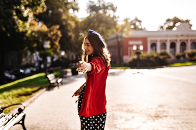 Foto de la parte de atrás de una chica con camisa roja de boina y falda de lunares caminando por la ciudad Arquitectura urbana durante un día cálido y soleado