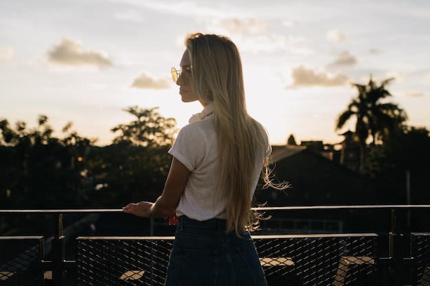 Foto gratuita foto de la parte posterior del modelo caucásico de pelo largo pasar tiempo al aire libre durante la puesta de sol.