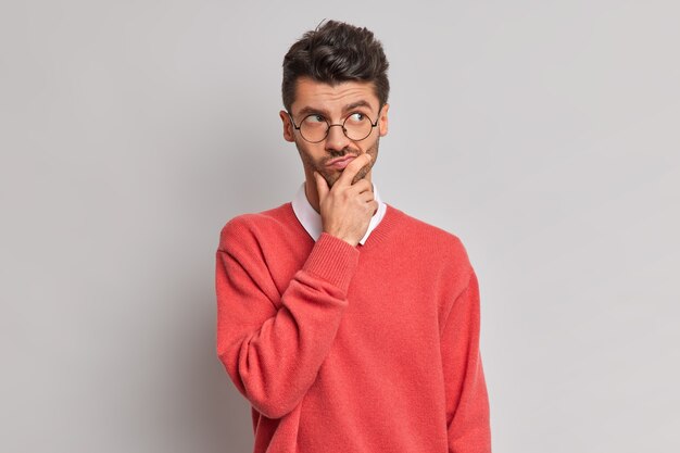 Foto de pensativo apuesto hombre europeo adulto sostiene la barbilla y mira pensativamente lejos intenta resolver el problema