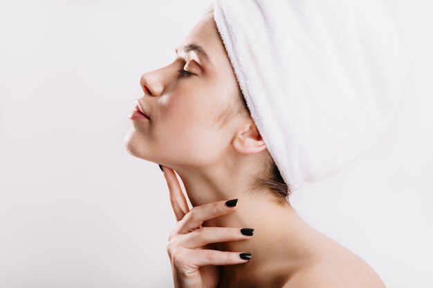 Foto de perfil de dama con toalla blanca en la cabeza. Mujer después de la ducha sin maquillaje posando en pared aislada.