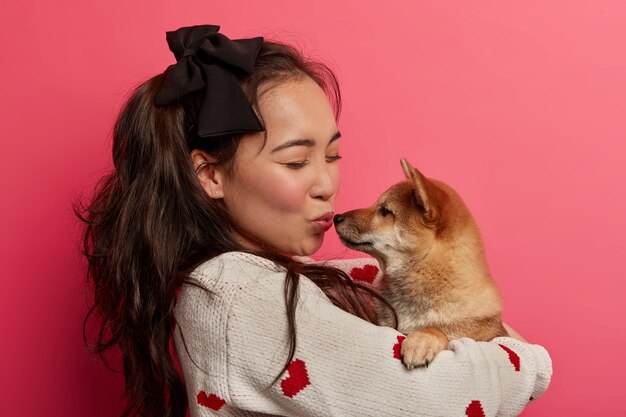 Foto de perfil de una mujer encantadora que abraza y besa al perro con amor, no ha visto a una mascota durante mucho tiempo, le gusta jugar con animales, aislado sobre el espacio rosa. Momento romantico