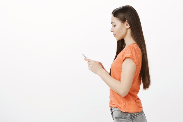 Foto de perfil de mujer morena bastante joven mediante teléfono móvil, compras en línea, mediante la aplicación de teléfono inteligente