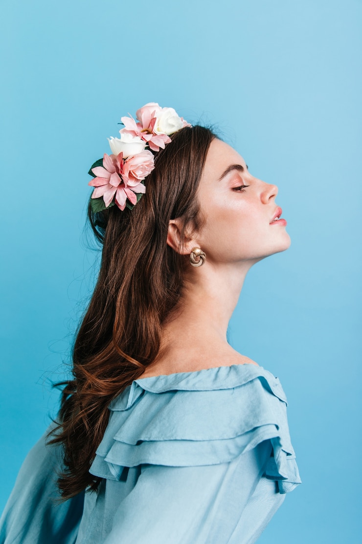 Foto gratuito foto de perfil de niña aristocrática en blusa con volantes. señora con flores en el pelo posando con orgullo contra la pared azul.