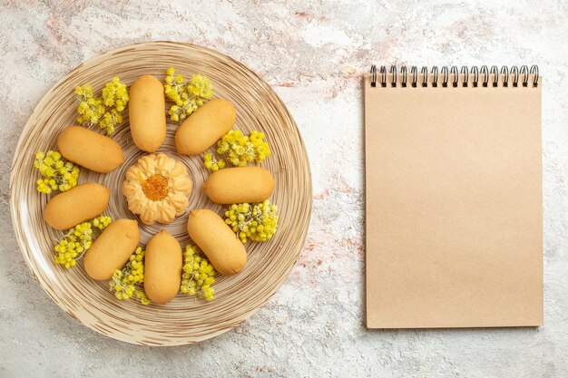 Foto de plato lleno de galletas con flores de color amarillo brillante y cuaderno