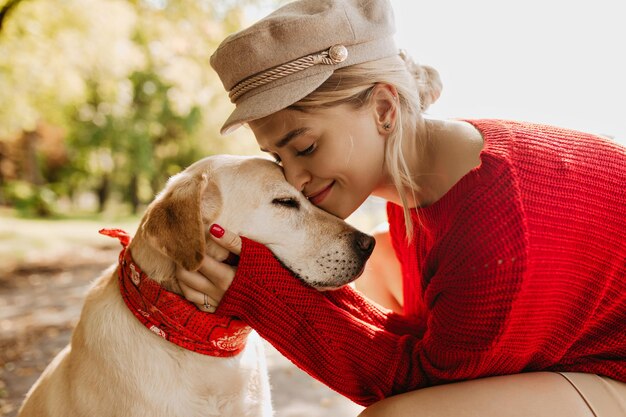 Foto de primer plano de una chica guapa y su perro sentados en otoño en el parque Encantadora rubia pasándola bien con su mascota