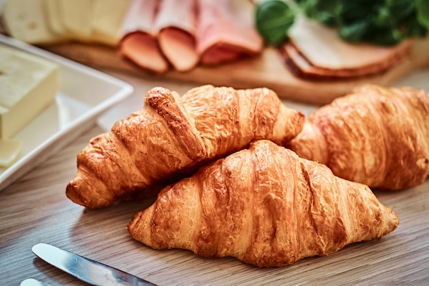 Foto de primer plano de un croissant con jamón, queso y mantequilla en una tabla de madera en una cocina.