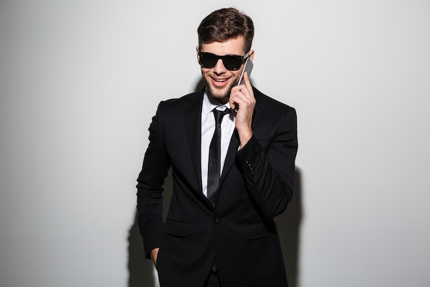 Foto de primer plano del empresario guapo sonriente con gafas hablando por teléfono móvil