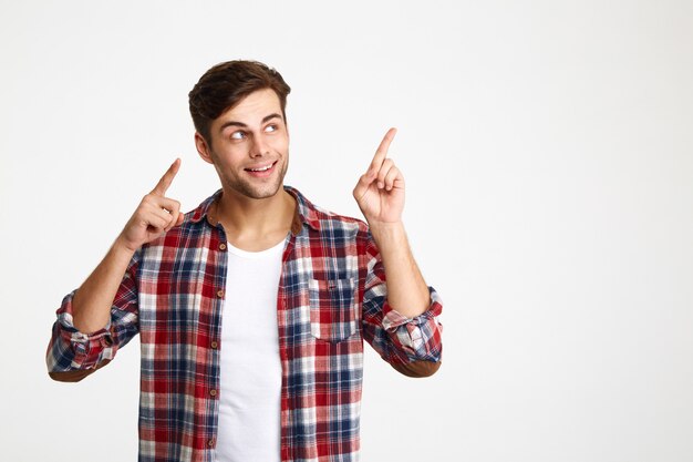 Foto de primer plano de feliz joven atractivo en camisa a cuadros apuntando con dos dedos, mirando a un lado