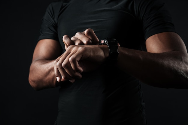 Foto de primer plano del hombre africano en camiseta negra, echa un vistazo a la hora en el reloj de pulsera negro