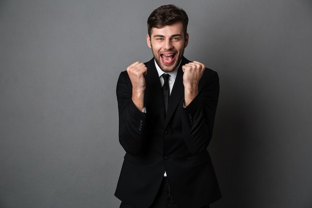 Foto de primer plano de hombre atractivo feliz en traje clásico mostrando gesto ganador,