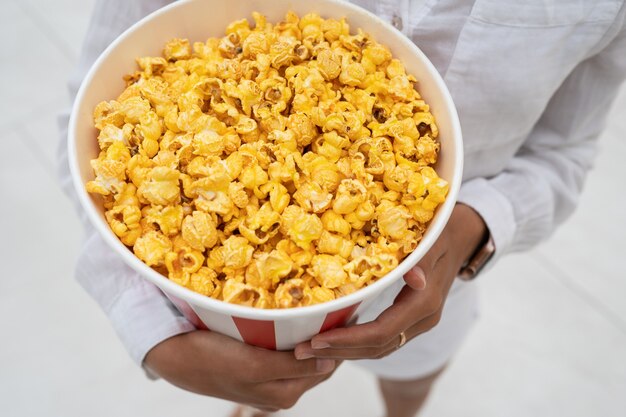 Foto de primer plano de una joven dulce, que sostiene un tubo de palomitas de maíz en sus manos.