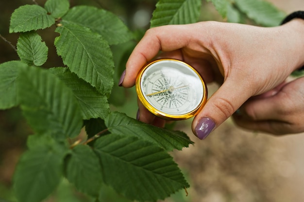 Foto de primer plano de manos femeninas con brújula junto a una rama de árbol