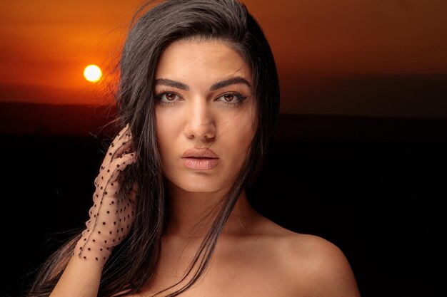 Foto de primer plano de la modelo caliente al atardecer poniendo su mano en su cabello Foto de alta calidad