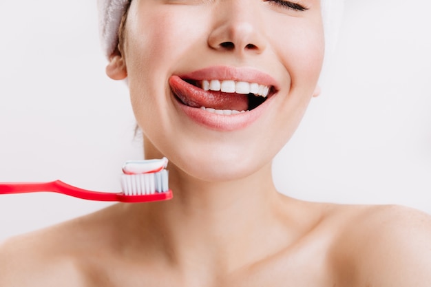 Foto de primer plano de mujer anticipando el cepillado de dientes. Modelo con sonrisa blanca como la nieve posando en la pared blanca.