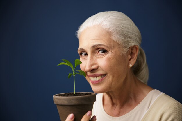 Foto de primer plano de mujer de edad feliz mostrando planta joven en el lugar