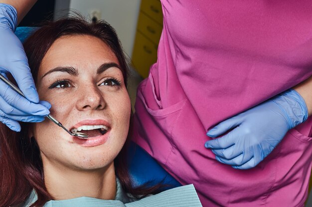 Foto de primer plano de una mujer joven que se examina mientras está sentada en la silla del dentista con la boca abierta.