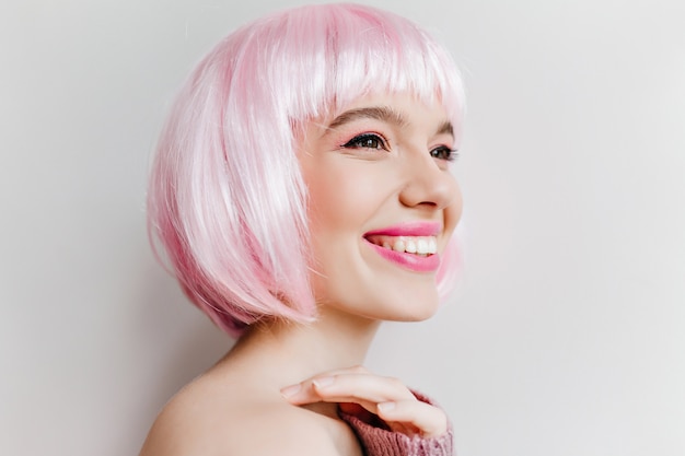 Foto de primer plano de refinada chica caucásica con ojos oscuros feliz riendo. Retrato de interior de mujer joven impresionante en periwig rosa disfrutando de la vida.