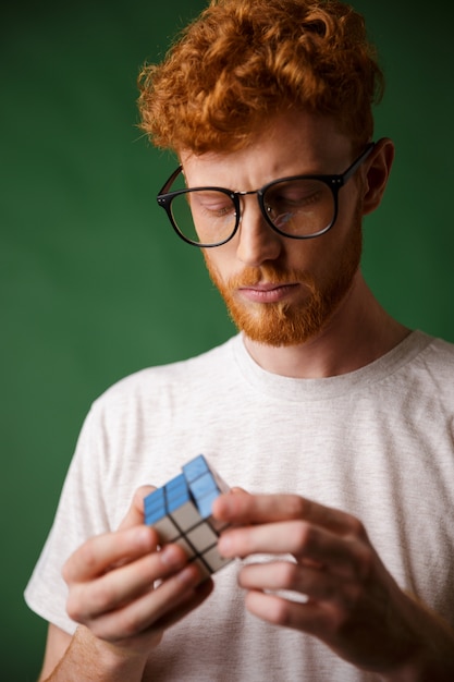 Foto de primer plano del tipo de cabeza lectora concentrada con gafas, jugando con el cubo de Rubic