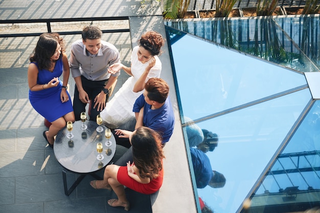 Foto principal del grupo de invitados a la fiesta sentados a la mesa con bebidas en la terraza