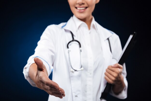 Foto recortada de alegre enfermera sosteniendo portapapeles y extender la mano