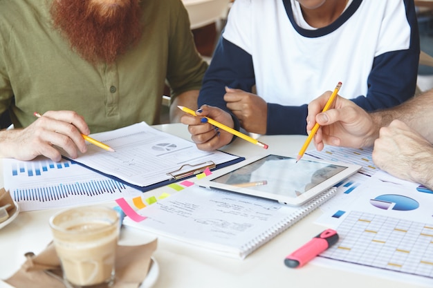 Foto recortada de compañeros de trabajo trabajando juntos y analizando cifras financieras en gráficos y diagramas.