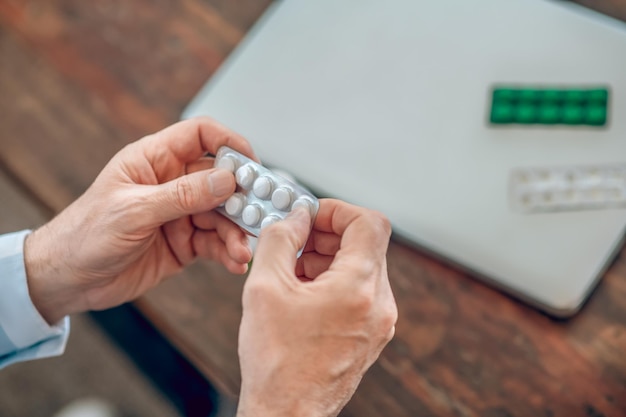 Foto recortada de dos manos masculinas caucásicas sosteniendo un blister con pastillas blancas redondas