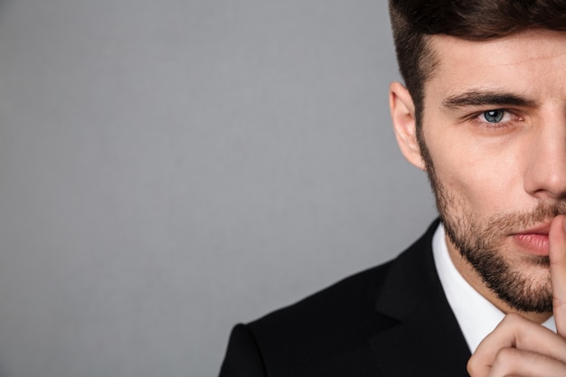 Foto recortada de guapo joven en chaqueta clásica mostrando gesto de silencio