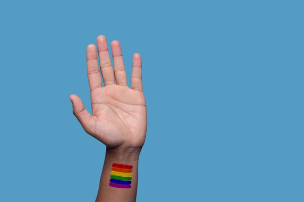 Foto recortada de un hombre adulto levantando la mano con el patrón de la bandera del arco iris en la muñeca