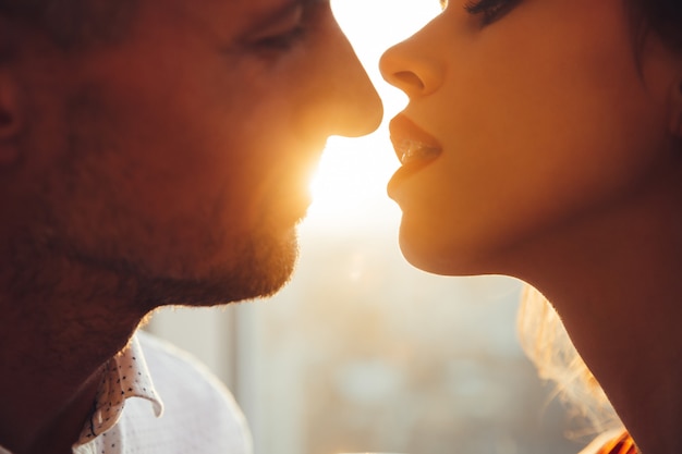 Foto recortada de jóvenes amantes besándose cerca de la ventana en casa