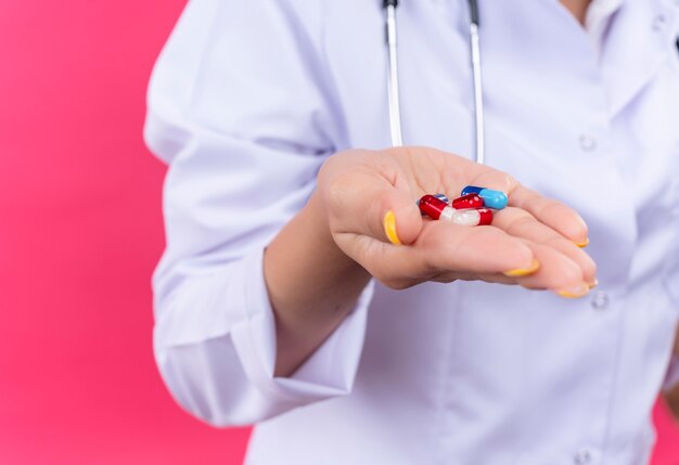 Foto recortada de la mano de la doctora con pastillas de colores sobre pared rosa