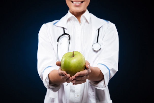 Foto recortada de mujer joven en bata médica con manzana verde