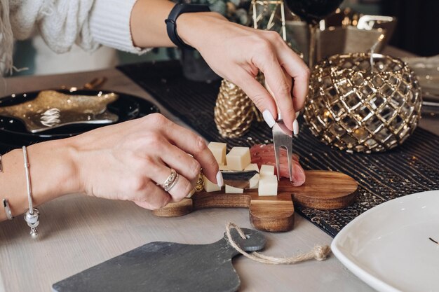 Foto recortada de mujer probando queso sobre una tabla de madera con adornos navideños en el fondo